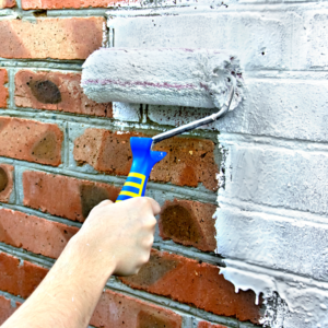 a closeup of a person painting the brick exterior of their house 